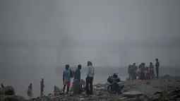 Orang-orang mandi dan melakukan ritual di sepanjang tepi sungai Yamuna di tengah kabut asap di New Delhi, India, Minggu (7/11/2021). Ibu kota New Delhi diselimuti udara beracun pada Sabtu kemarin karena tingkat polusi yang sangat tinggi pasca-perayaan festival besar agama Hindu. (Money SHARMA/AFP)