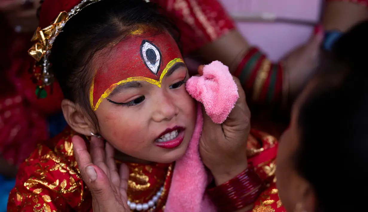 Seorang wanita membersihkan wajah seorang gadis muda yang berpakaian seperti dewi hidup Kumari saat menunggu Kumari Puja, sebuah ritual pemujaan di Hanuman Dhoka, Basantapur Durbar Square, Kathmandu, Nepal, Rabu, 27 September 2023. (AP Photo/Niranjan Shrestha)