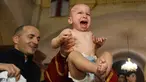 Seorang bayi menangis saat pendeta mengangkatnya dari air dalam acara pembaptisan massal di Gereja Katedral Holy Trinity, Tbilisi, Georgia (21/1). (AFP Photo/Vano Shlamov)