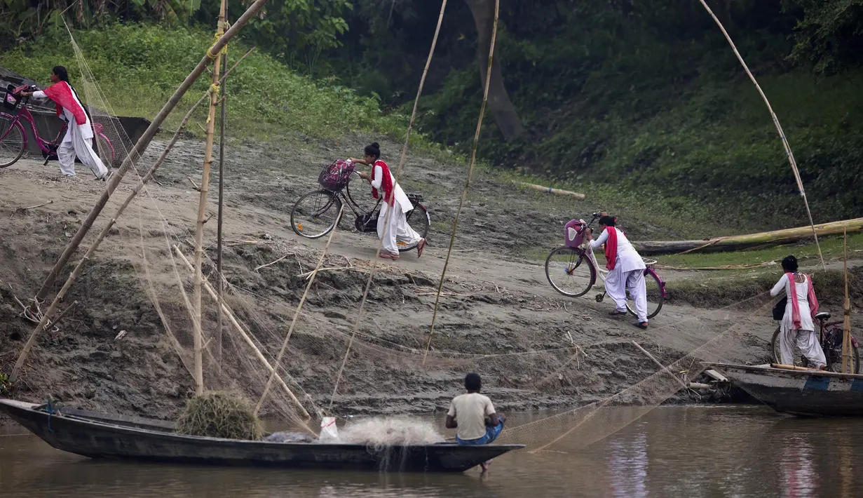 Siswa sekolah mendorong sepeda mereka ke atas bukit setelah menyeberangi sungai Brahmaputra di atas kapal di desa Kasoshila di pinggiran Gauhati, India (21/10/2019).  (AP Photo/Anupam Nath)