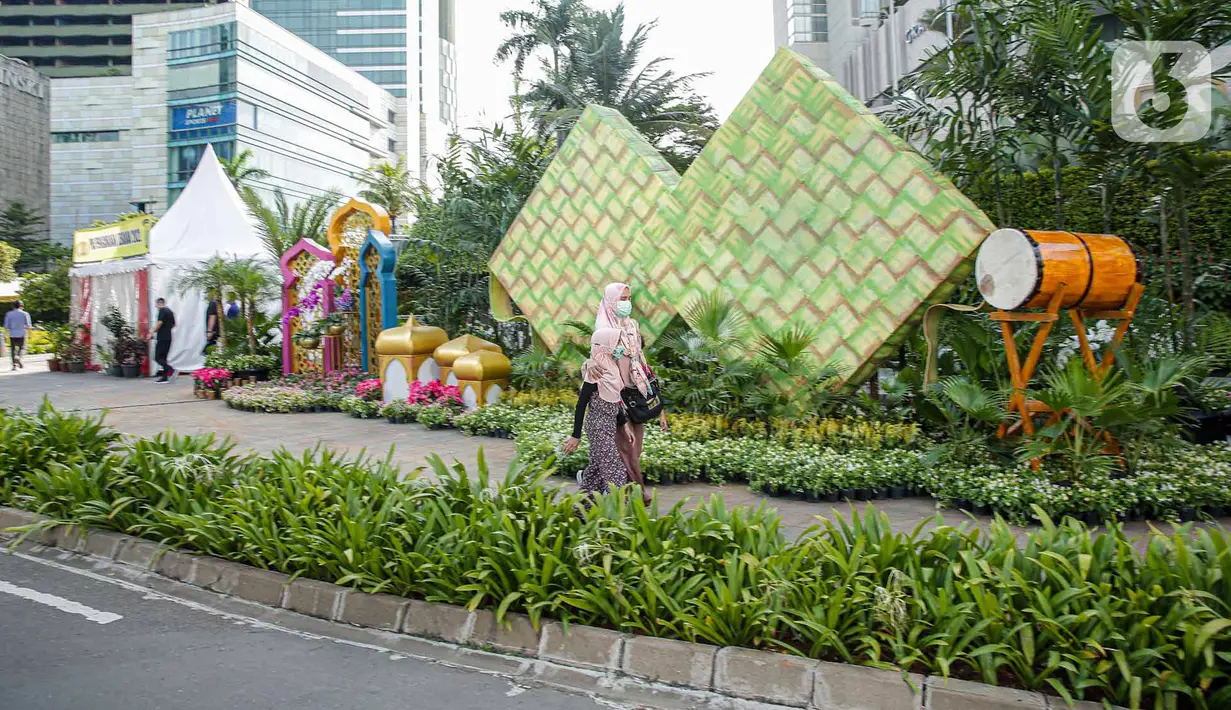 <p>Sejumlah warga berjalan melewati dekorasi bertemakan Idul Fitri di kawasan Bundaran HI, Jakarta, Rabu (27/4/2022). Dekorasi berbentuk masjid, ketupat, dan bedug yang dihiasi oleh tanaman tersebut dalam rangka menyambut Idul Fitri 1443 Hijriah. (Liputan6.com/Faizal Fanani)</p>