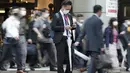Seorang komuter melihat ponselnya saat orang-orang berjalan selama jam sibuk di Stasiun Shinagawa, Tokyo, Jumat (1/10/2021). Pemerintah Jepang mencabut keadaan darurat di semua wilayah pada 1 Oktober 2021. (AP Photo/Eugene Hoshiko)