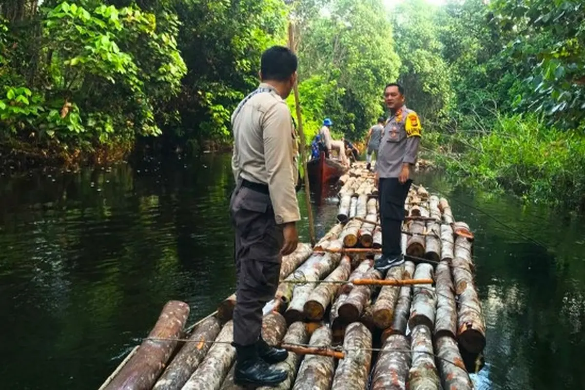 Personel Polres Siak berdiri di atas rakit yang merupakan pohon hasil pembalakan liar.