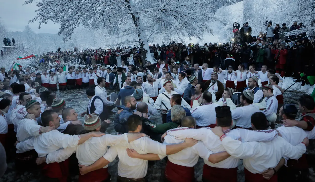 Sejumlah pria Bulgaria menari bersama di perairan sungai Tundzha selama perayaan Hari Epiphany di kota Kalofer, Bulgaria (6/1). Ritual ini merupakan pembersihan diri dari dosa-dosa selama setahun. (AP Photo/Valentina Petrova)