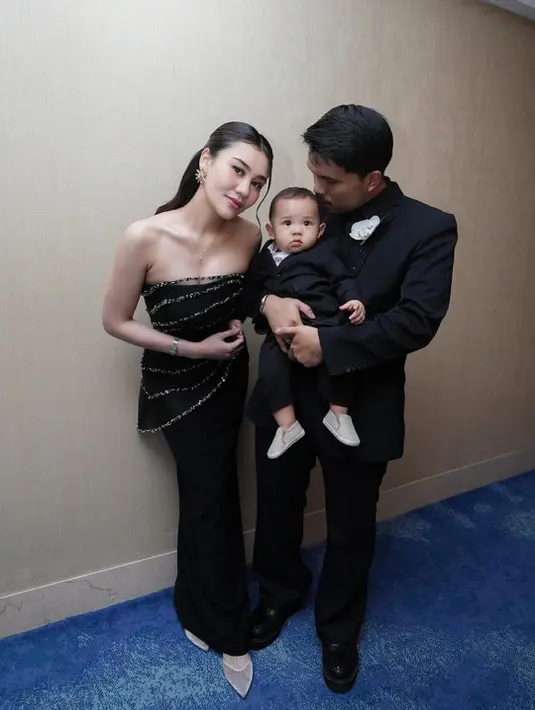 Aaliyah tampil anggun dalam strapless black gown beraksen detail berkilau yang memberi sentuhan glam tanpa berlebihan. Thariq memilih setelan jas hitam klasik dengan boutonniere putih, terlihat kontras sekaligus rapi. Kehadiran sang buah hati yang juga mengenakan busana hitam membuat tampilan keluarga kecil ini terlihat sangat kompak dan manis. [@aaliyah.massaid].