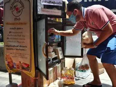 Seorang pria mengumpulkan barang-barang yang disumbangkan oleh publik pada “Pantry of Sharing” di Bangkok, Rabu (13/5/2020). Warga mendirikan lemari dapur berisi deretan produk di pinggir- pinggir jalan untuk membantu yang lain di tengah krisis Covid-19. (Lillian SUWANRUMPHA/AFP)