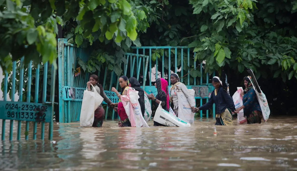 Orang-orang melintasi jalan yang tergenang air setelah hujan monsun di Gurgaon di pinggiran New Delhi (19/8/2020). Hujan lebat melanda New Delhi pada 19 Agustus, membanjiri jalan dan menumpuk kesengsaraan bagi penumpang di ibu kota India yang kacau balau. (AFP/Xavier Galiana)