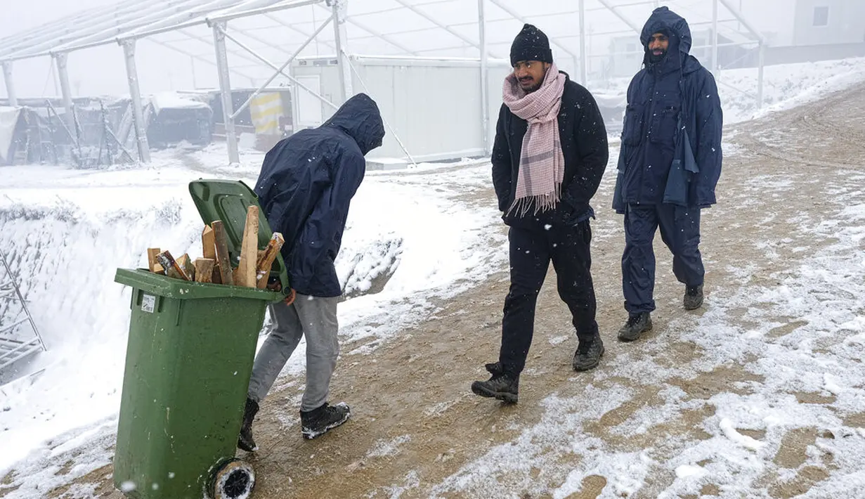 Seorang imigran membawa kayu bakar dalam tempat sampah di Kamp Lipa, luar Bihac, Bosnia, Jumat (8/1/2021). Cuaca bersalju dan musim dingin telah membawa lebih banyak penderitaan bagi ratusan imigran yang terjebak selama berhari-hari di kamp tersebut. (AP Photo/Kemal Softic)