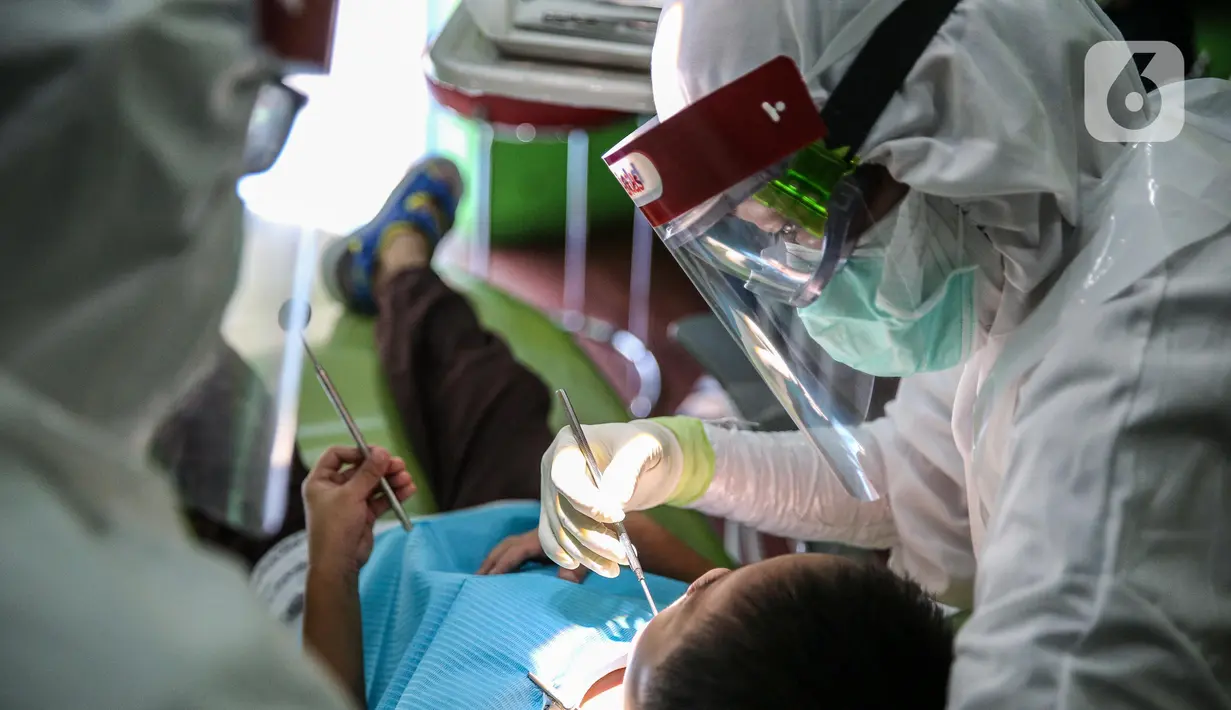 Dokter menggunakan APD memeriksa gigi pasien anak di klinik Medikids kawasan Kemang, Jakarta Selatan, Selasa (7/7/2020). Pelayanan dokter gigi dengan menggunakan APD lengkap  untuk memenuhi protokol kesehatan guna mencegah penyebaran covid-19 di era kenormalan baru. (Liputan6.com/Faizal Fanani)