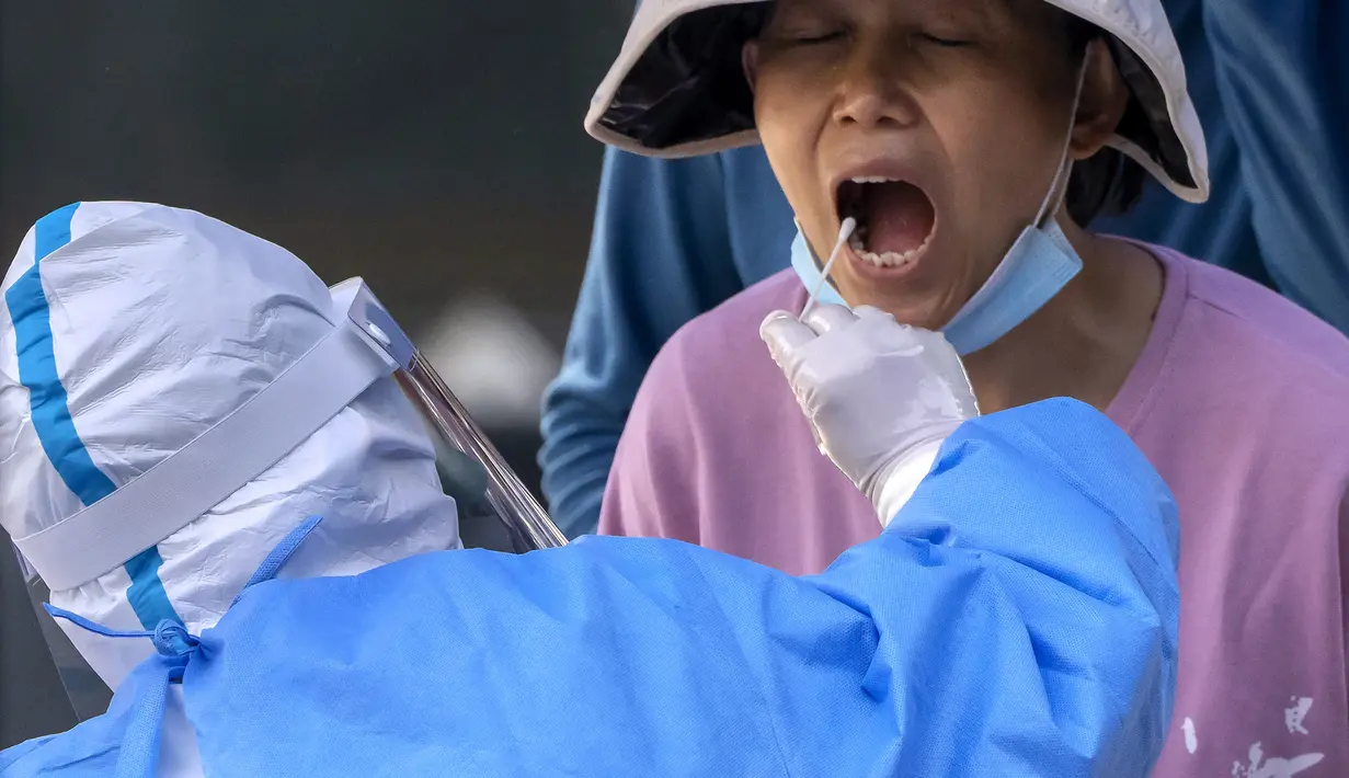 <p>Seorang pekerja yang mengenakan pakaian pelindung menyeka tenggorokan seorang wanita untuk tes COVID-19 pada hari ketiga berturut-turut tes virus corona massal di Beijing, Kamis (5/5/2022). Ibu kota China Beijing pada Kamis (5/5) mulai melonggarkan aturan karantina untuk kedatangan dari luar negeri. (AP Photo/Mark Schiefelbein)</p>