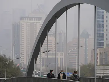 Orang-orang yang memakai masker untuk membantu mengekang penyebaran virus corona berjalan di atas jembatan di atas gedung perkantoran yang diselimuti kabut polusi di Beijing, Kamis (18/11/2021).  (AP Photo/Andy Wong)