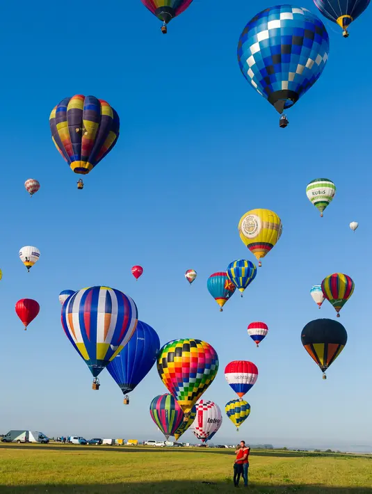 Sepasang kekasih berpelukan saat ratusan balon udara terbang di pangkalan udara Chambley-Bussieres, Hagéville, Prancis, Senin (29/7/2019). Acara ini disebut sebagai salah satu ajang pertemuan para pilot balon udara terbesar di dunia. (Jean-Christophe VERHAEGEN/AFP)