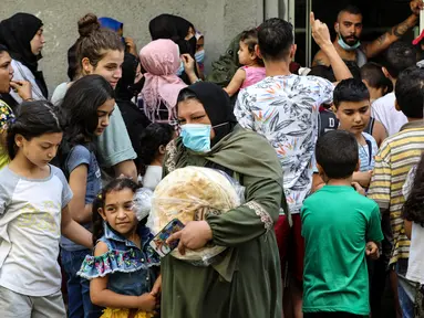 Seorang perempuan meninggalkan toko roti saat orang-orang menunggu giliran, di lingkungan Nabaa, Beirut, Jumat (13/8/2021). Tanpa masker, warga Lebanon berbondong-bondong ke toko roti sebelum fajar untuk membeli roti yang terjangkau ketika pasokan bahan bakar dan obat-obatan terbatas. (ZAYYAT/AFP)