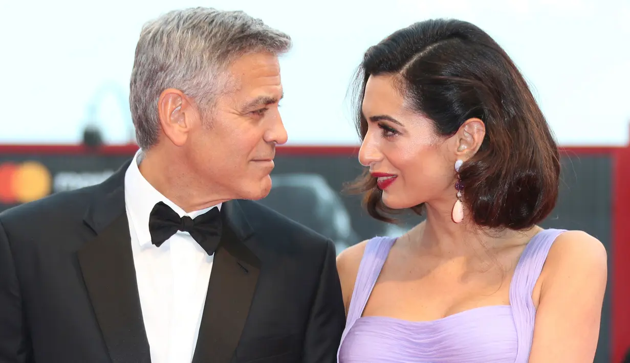 Pasangan selebritis, George dan Amal Clooney berpose untuk fotografer di Venice Film Festival ke-74, Italia, 2 September 2017.  Sentuhan glamor Amal semakin terasa berkat anting berbatu safir dan giok dari Lorraine Schwartz. (Joel Ryan/Invision/AP)
