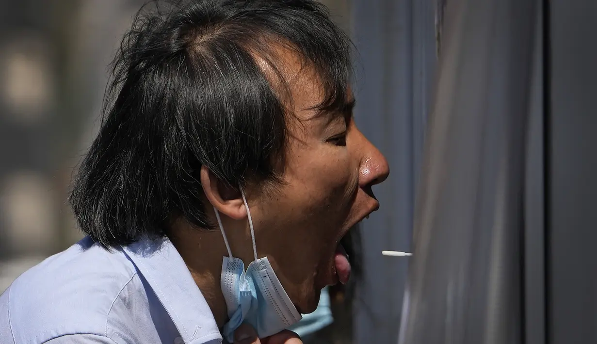 Seorang pekerja menarik maskernya untuk sampel swab tenggorokan di tempat pengujian virus corona di Beijing, Minggu (3/4/2022). Kasus COVID-19 di kota terbesar di China, Shanghai, masih meningkat saat jutaan orang tetap terisolasi di rumah di bawah lockdown besar-besaran. (AP Photo/Andy Wong)
