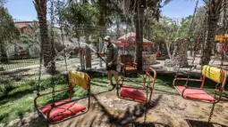 Seorang pekerja mengenakan masker menyiram tanah dan kursi komedi putar di kebun binatang lokal Palestina di Rafah di Jalur Gaza selatan (26/5/2020). Kebun binatang itu ditutup selama liburan Idul Fitri karena pandemi virus coronavirus COVID-19. (AFP/Said Khatib)