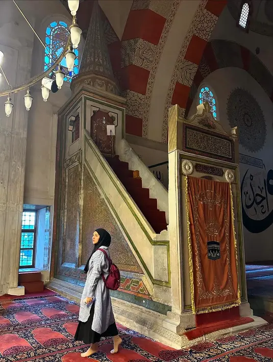 Berkunjung ke masjid tertua di Turki, Eski Ulu Camii, Irish Bella tampil dengan kemeja tunik panjang warna biru muda, dipadukan maxi skirt hitam, dan tas merahnya. [@_irishbella_]