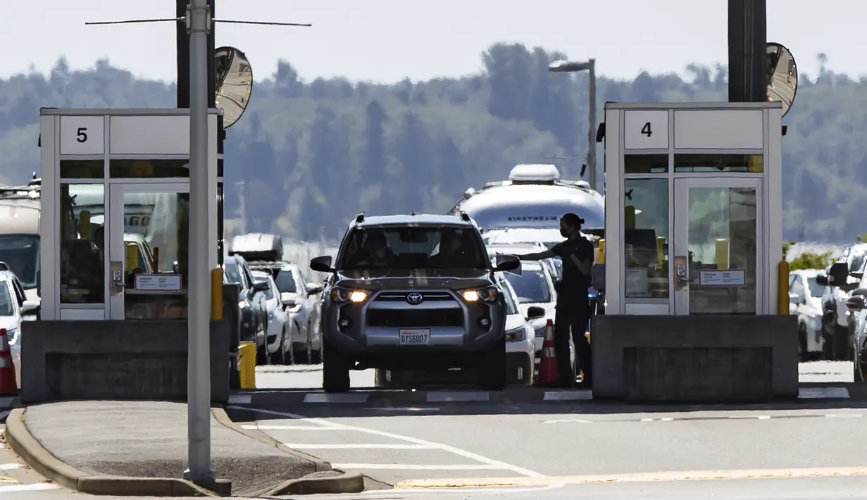 Petugas Badan Layanan Perbatasan Kanada menyerahkan dokumen ke pengendara yang memasuki Kanada di perbatasan Douglas-Peace Arch, Surrey, British Columbia, Kanada, Senin (9/8/2021). Kanada mencabut larangan terhadap warga AS melintasi perbatasaan negaranya. (Darryl Dyck/The Canadian Press via AP)