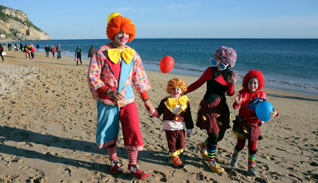 Sebuah keluarga mengenakan kostum badut berjalan di pantai saat mengikuti Parade Karnaval Clowns di pantai Sesimbra, Lisbon, Spanyol (12/2). Karnaval ini digelar setiap tahun dan jatuh pada hari Senin. (AP Photo / Armando Franca)