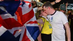Suporter berbaju Inggris dan Ukraina berciuman saat merayakan kemenangan Timnas Inggris pada akhir pertandingan sepak bola Perempatfinal EURO 2020 antara Inggris melawan Ukraina, di depan Stadion Olimpiade, Roma pada 3 Juli 2021.
(AFP/Andreas Solaro)