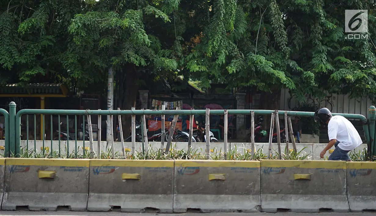Warga menyeberang melalui pagar pembatas jalur transjakarta yang ditopang bambu di Jalan Otista Raya, Jakarta, Jumat (5/7/2019). Meskipun telah lama rusak, pagar yang berfungsi sebagai pembatas agar orang tidak menyeberang secara sembarangan itu belum juga diperbaiki (Liputan6.com/Immanuel Antonius)
