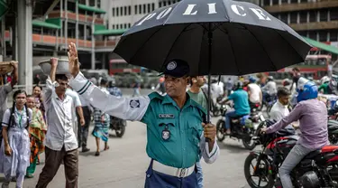 Seorang petugas polisi Bangladesh memegang payung untuk melindungi dirinya dari sengatan matahari saat mengatur lalu lintas di persimpangan jalan di Dhaka pada tanggal 12 Agustus 2024. (LUIS TATO/AFP)