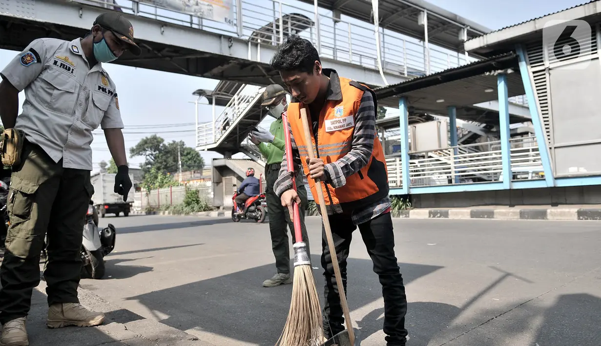 Seorang warga membersihkan jalanan saat menjalani hukuman sosial pelanggar PSBB di area Pasar Kramat Jati, Jakarta, Rabu (17/6/2020). (merdeka.com/Iqbal S. Nugroho)