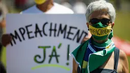 Pengunjuk rasa memegang poster bertuliskan "Impeachment Now" saat aksi protes terhadap Presiden Brasil Jair Bolsonaro dan penanganan virus corona di Brasilia, pada Minggu (31/1/2021). Di antara mereka banyak yang menuntut pengunduran diri atau pemakzulan Presiden Jair Bolsonaro. (Sergio LIMA/AFP)