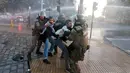 Polisi anti huru hara menarik dua orang pria saat terjadi unjuk rasa di luar kedutaan AS di Santiago, Chili (14/4). Serangan itu menyisakan puing-puing bangunan yang luluh lantak akibat rudal. (AP / Esteban Felix)