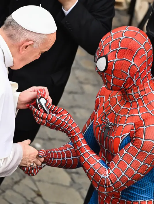 Seorang pria yang mengenakan kostum Spider-Man menyerahkan maskernya kepada Paus Fransiskus saat mereka bertemu di akhir audiensi umum mingguan di San Damaso Courtyard, Vatikan, Rabu (23/6/2021). Pria itu adalah Mattia Villardita (27) yang menghibur anak-anak di rumah sakit. (Alberto PIZZOLI / AFP)