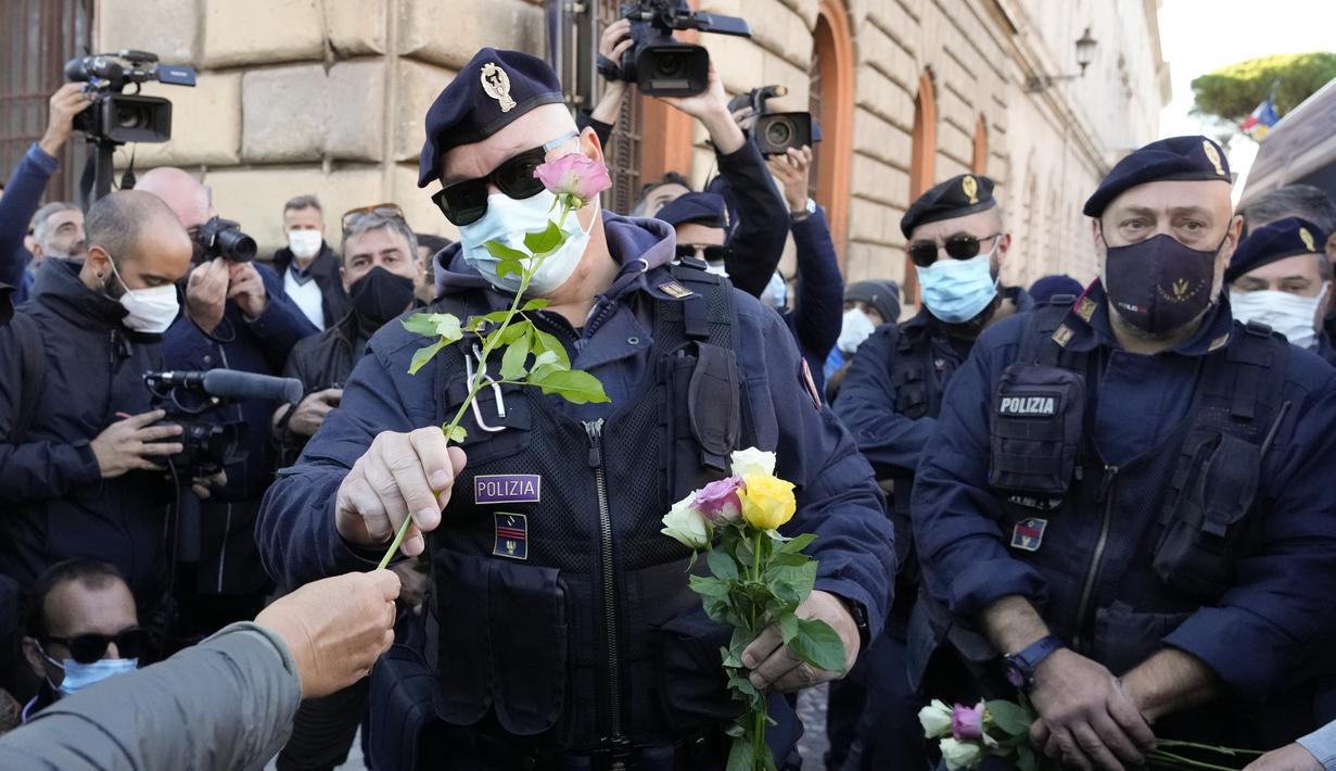 Petugas polisi menerima bunga yang diberikan demonstran selama aksi protes di Circus Maximus Roma, Jumat (15/10/2021). Protes tersebut karena aturan yang mengharuskan seluruh pekerja di Italia menunjukkan kartu kesehatan covid-19 untuk memasuki tempat kerja mereka. (AP Photo/Gregorio Borgia)