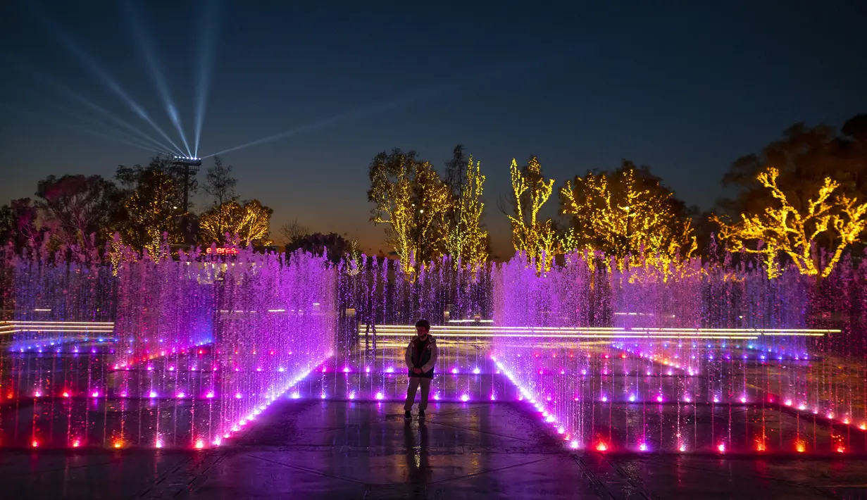Seorang anak laki-laki berdiri di dalam pertunjukan cahaya dan air Natal yang ditampilkan di Experience Park, di distrik pesisir Hellenikon di Athena, Yunani, Senin (20/12/2021).  (AFP/Angelos Tzortzinis)