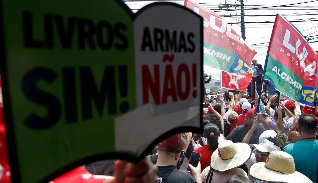 Sebuah tanda bertuliskan "Buku Ya, Tidak Senjata" terlihat saat mantan presiden Brasil (2003-2010) dan calon presiden dari Partai Buruh (PT) berhaluan kiri, Luiz Inacio Lula da Silva (kanan), menyampaikan pidato saat kampanye di Sao Mateus, Negara Bagian Sao Paulo, Brasil, Senin (17/10/2022). Lula da Silva dan presiden Jair Bolsonaro akan menghadapi putaran kedua pemilihan presiden pada 30 Oktober, dengan ekspektasi persaingan ketat mendorong kedua belah pihak untuk mengintensifkan kampanye di putaran kedua. (Miguel SCHINCARIOL / AFP)