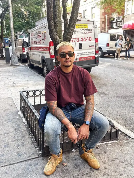 Duduk santai di pinggir jalan kota New York, UUS tampil kasual mengenakan kaos polos Erigo dipadu celana jeans dan high up sneakers berwarna coklat. (Instagram/uusbiasaaja).