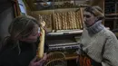 Pemilik toko roti Florence Poirier (kiri) mencium aroma baguette baru yang keluar dari oven saat Mylene Poirier berdiri di sampingnya di sebuah toko roti, di Versailles, sebelah barat Paris, Selasa, 29 November 2022. Meskipun konsumsi baguette telah menurun selama beberapa dekade terakhir, Prancis masih menghasilkan sekitar 16 juta roti per hari - hampir 6 miliar baguette setahun - menurut perkiraan Fidusia 2019. (AP Photo/Michel Euler)