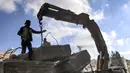 Seorang pekerja Palestina berdiri di samping balok-balok beton rusak yang ditarik oleh derek sebagai bagian dari penyelamatan bahan konstruksi bangunan yang hancur selama konflik Mei 2021 antara Hamas dan Israel di Kota Gaza, Sabtu (5/6/2021). (MAHMUD HAMS/AFP)