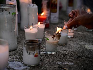 Seorang wanita menyalakan lilin untuk memberikan penghormatan kepada para korban tewas di depan klub malam Jet Set di Santo Domingo, Dominika pada 11 April 2025. (MARTIN BERNETTI/AFP)