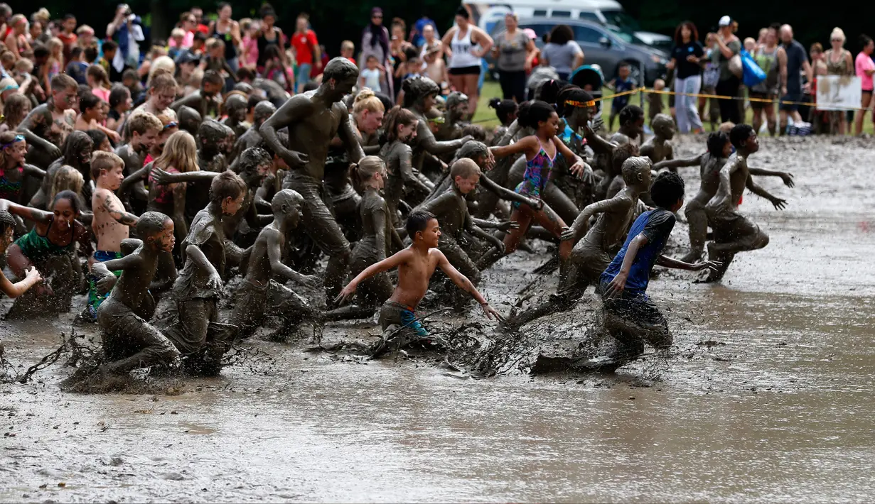 Ratusan anak berlari ke dalam lubang lumpur berisi ratusan ton lumpur saat perayaan Mud Day di Nankin Mills Park di Westland, Michigan, AS (11/7). (AFP Photo/Jeff Kowalsky)