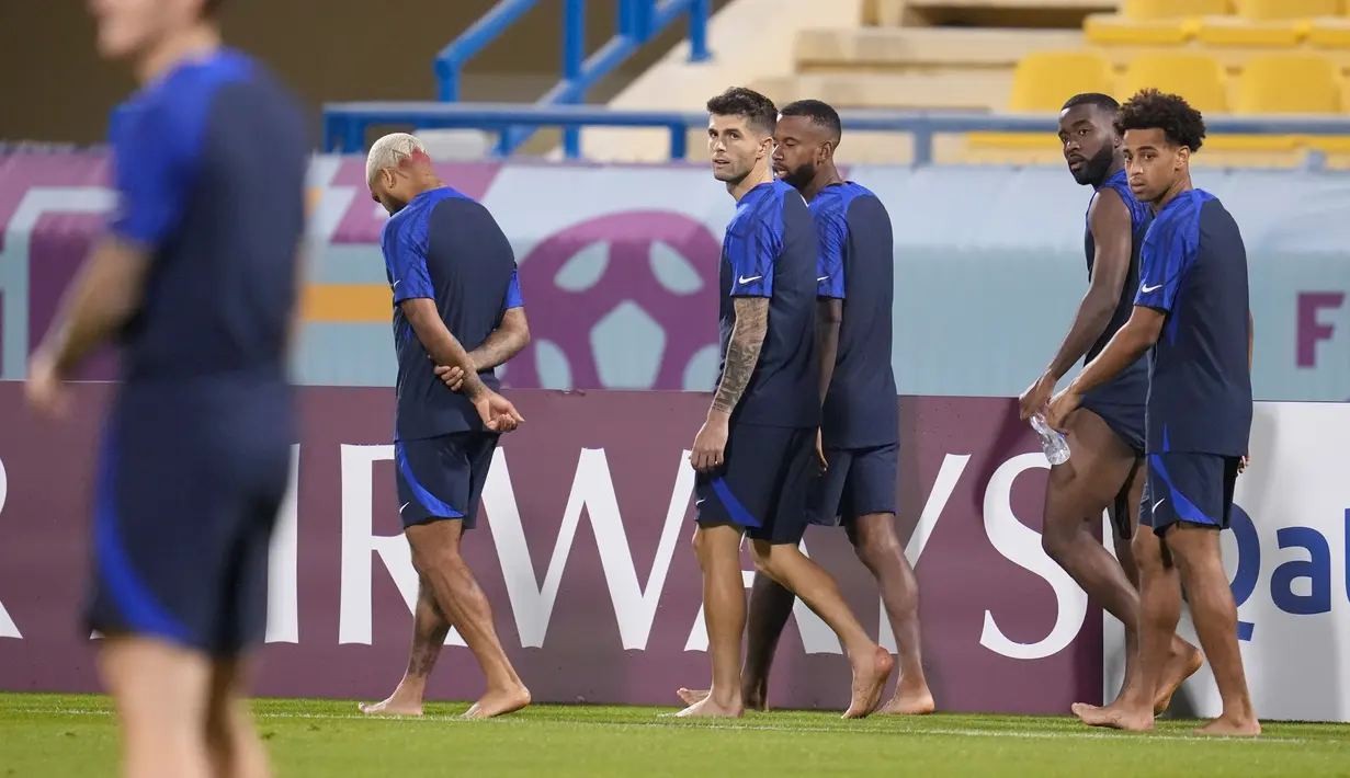 Kapten timnas AS Christian Pulisic (tengah) dan pemain lain berjalan tanpa alas kaki di lapangan selama sesi latihan resmi di Stadion Al-Gharafa SC, Doha, Senin (28/11/2022). Pertandingan AS vs Iran ini diprediksi akan berlangsung panas karena memperebutkan posisi 16 besar Piala Dunia 2022. (AP Photo/Ashley Landis)