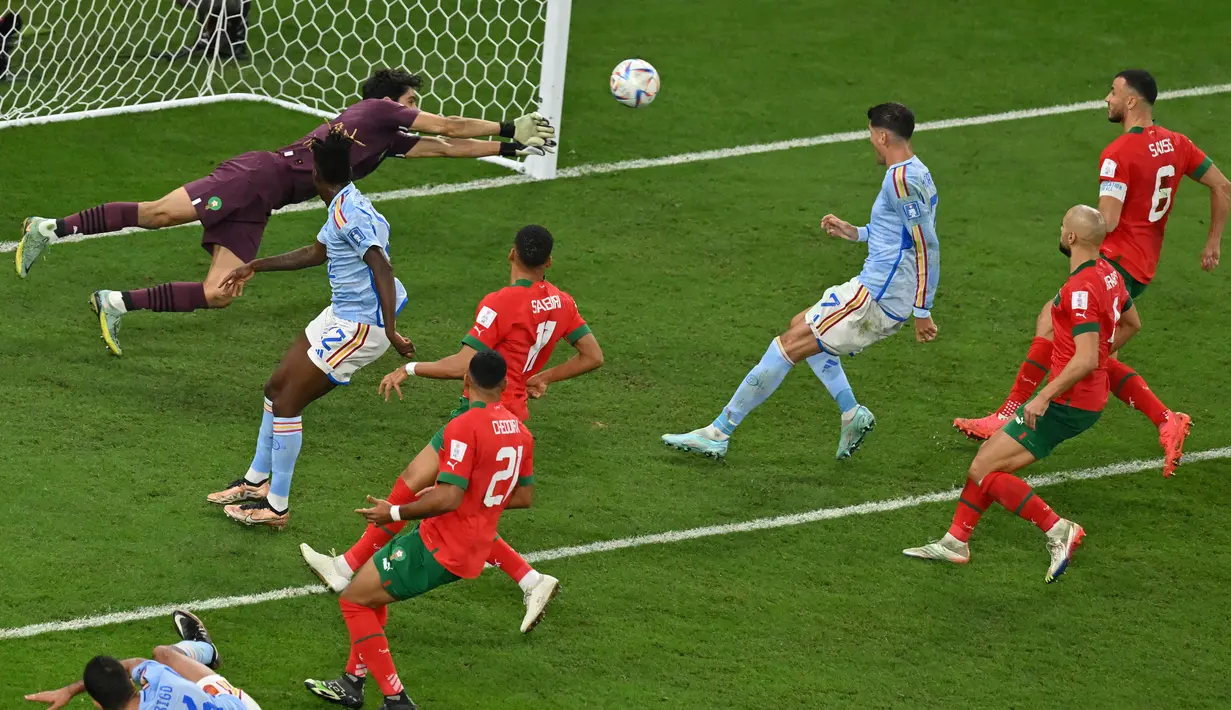 Kiper Maroko #01 Yassine Bounou membelokkan bola dari serangan pemain Spanyol pada babak 16 besar Piala Dunia 2022 di Education City Stadium, Al Rayyan, Rabu (6/12/2022) dini hari WIB. Lanjut ke babak adu penalti, Yassine Bounou kiper Maroko tampil luar biasa dengan menepis tiga penalti lawan. (Glyn KIRK / AFP)