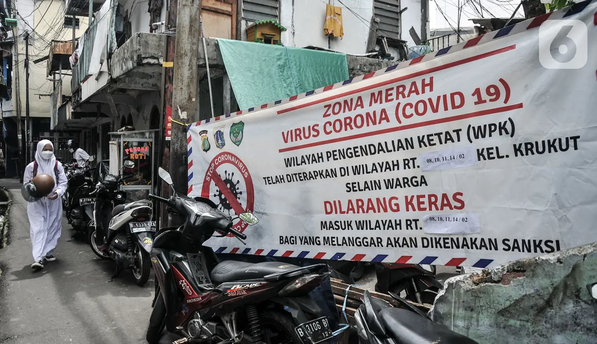 Seorang pelajar melintas dekat spanduk yang digunakan untuk menutup wilayah RW 002, Kelurahan Krukut, Taman Sari, Jakarta Barat, Senin (10/1/2022). Selain mikro lockdown, petugas melakukan tes massal kepada warga setempat guna mencegah penularan COVID-19 lebih luas. (merdeka.com/Iqbal S. Nugroho)