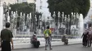 Orang-orang berjalan di samping air mancur di Yangon saat militer menahan pemimpin de facto Myanmar Aung San Suu Kyi dan presiden Myint dalam kudeta, Senin (1/2/2021). Militer Myanmar mengatakan penahanan dilakukan untuk merespons kecurangan pemilu 2020 yang dimenangkan Suu Kyi. (AP Photo/Thein Zaw)