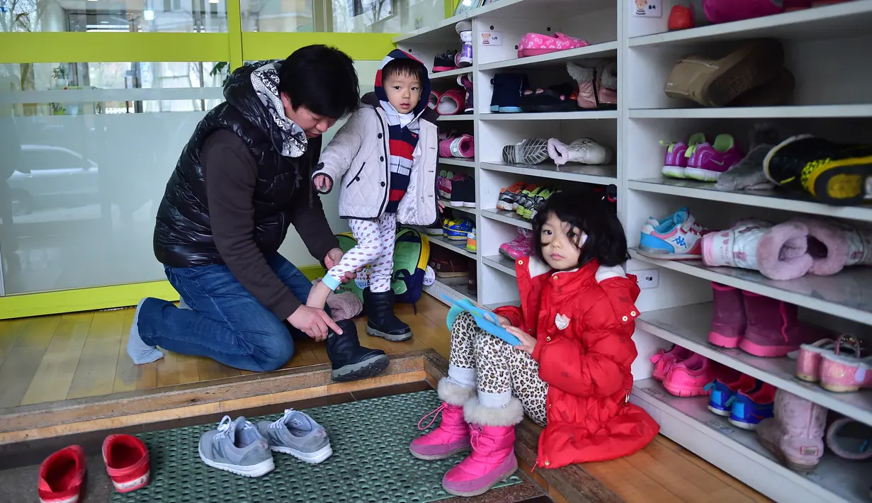 Kim Jin-Sung memakaikan sepatu anaknya Won-Woo di perawatan anak di Seoul. Kim adalah salah satu dari meningkatnya jumlah ayah di Korea Selatan memilih istirahat dari karirnya untuk membantu membesarkan anak-anaknya. (AFP PHOTO/JU)