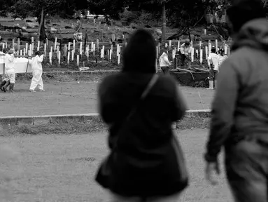Kerabat dan keluarga menyaksikan dari kejauhan proses pemakaman jenazah dengan protokol COVID-19 di TPU Bambu Apus, Jakarta, Kamis (28/1/2021). Hingga Kamis (28/1), di Indonesia, jumlah orang yang meninggal dunia akibat terpapar COVID-19 berjumlah 29.331 jiwa. (Liputan6.com/Helmi Fithriansyah)