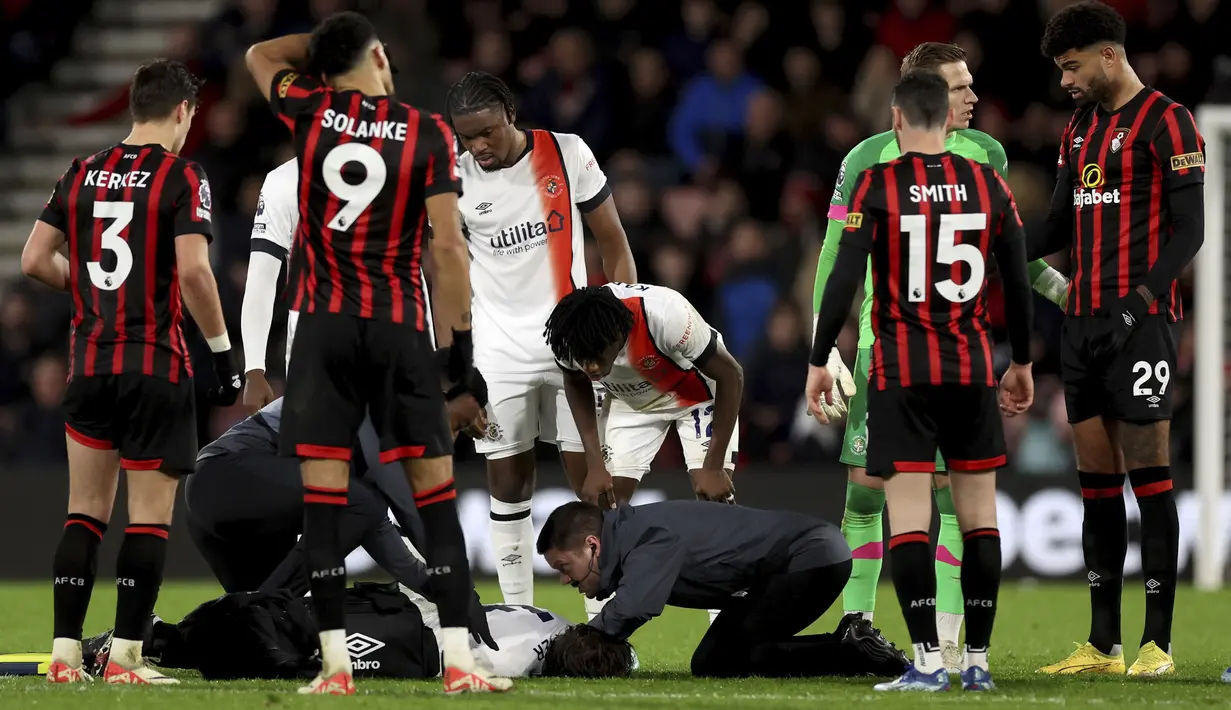 Petugas medis menolong pemain Luton Town, Tom Lockyear yang mengalami pingsan secara tiba-tiba di tengah lapangan dalam pertandingan Liga Inggris 2023/2024 antara Bournemouth melawan Luton Town yang berlangsung di Vitality Stadium, Sabtu (16/12/2023). (AP/PA/Steven Paston)
