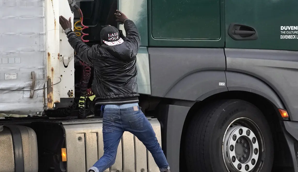 Migran melompati truk untuk mencoba menyeberangi terowongan menuju Inggris di Calais, Prancis pada 14 Oktober 2021. Dalam praktik berbahaya dan berpotensi mematikan, ia mencoba melewati terowongan yang dijaga ketat yang menghubungkan kedua negara dengan bersembunyi di truk. (AP/Christophe Ena)