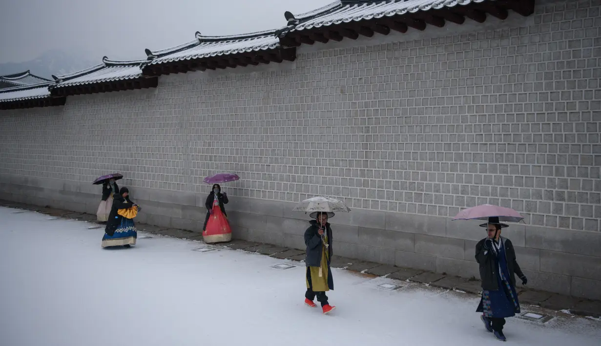 Pengunjung mengenakan gaun hanbok tradisional berjalan di sepanjang dinding istana Gyeongbokgung saat hujan salju di pusat kota Seoul, Korea Selatan (13/12). (AFP Photo/Ed Jones)
