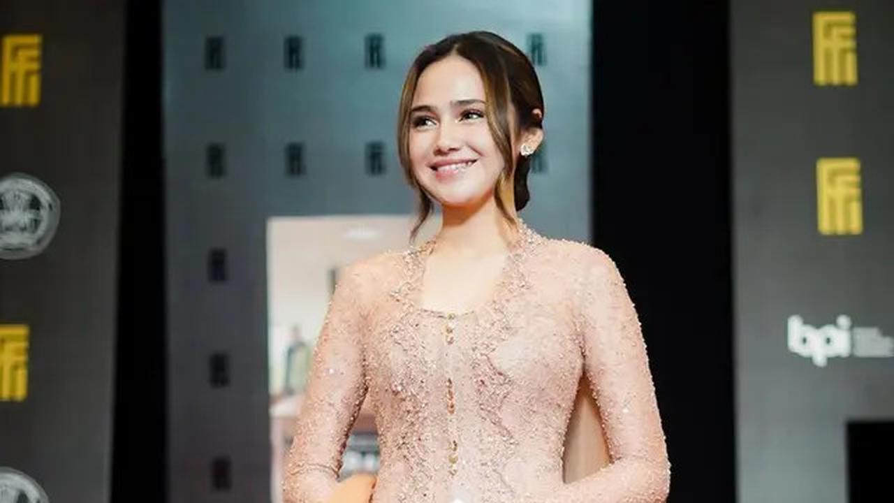 Syifa tampil menawan dengan kebaya panjang brokat, kain lilit coklat, dan selendang tuller karya desainer Fadlan.