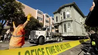 Pekerja memberi arahan kepada sopir truk yang sedang menarik rumah bergaya Victoria berusia 139 tahun di San Francisco, Minggu (21/2/2021). Rumah dua lantai yang dibangun pada tahun 1882 tersebut dipindahkan ke lokasi baru yang berjarak hanya enam blok.  (AP Photo/Noah Berger)