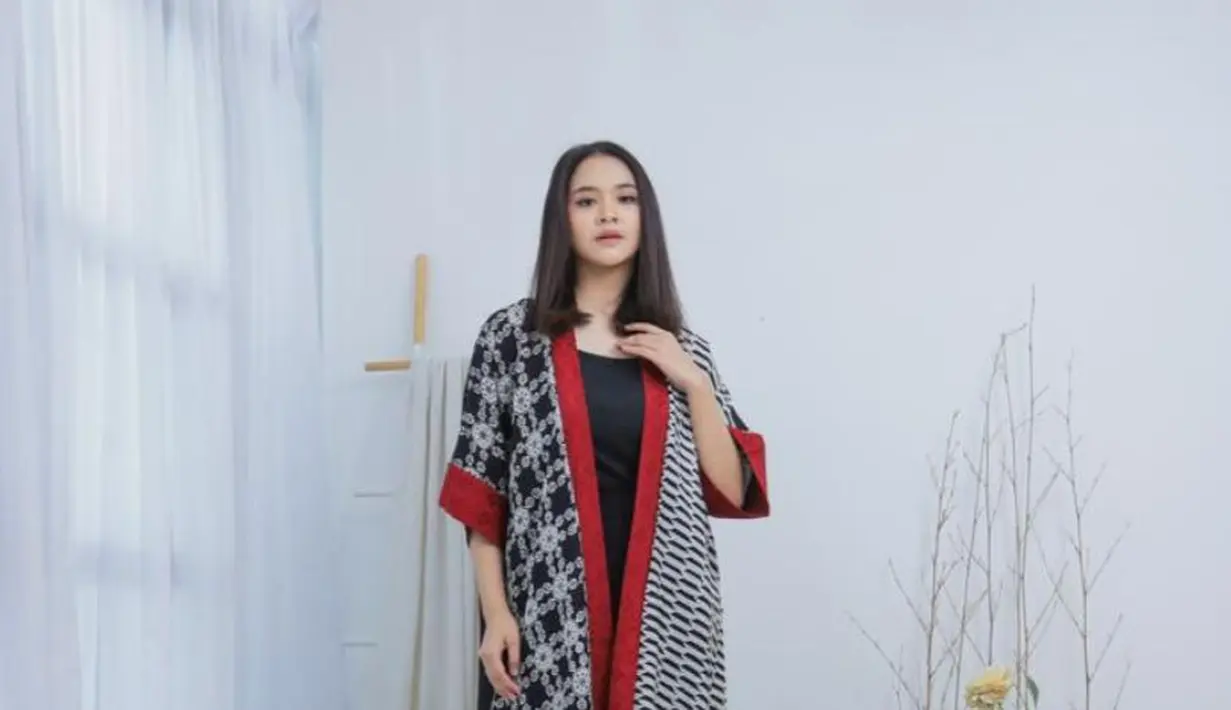 Memadukan dua motif batik berwarna hitam-putih, menghadirkan harmoni visual yang unik. Sentuhan aksen merah pada bagian tepi depan dan ujung lengan menjadi poin statement yang memberi kesan berani dan elegan. [Dok/MAMAUTY]